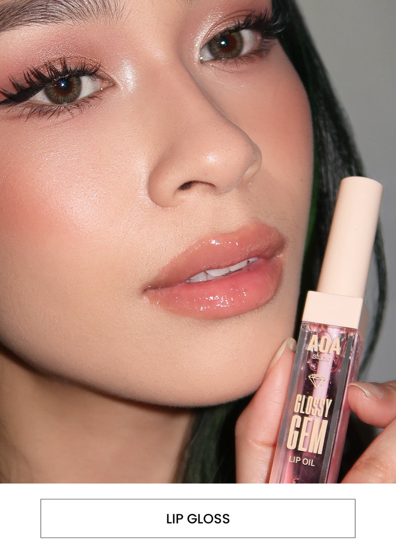 Image of a woman wearing lip gloss and holding an AOA Glossy Gem Lip Gloss Tube alongside a “Lip gloss” button