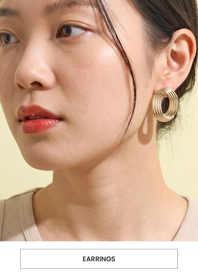 Image of a woman wearing golden abstract earring hoops alongside a “Earrings” button
